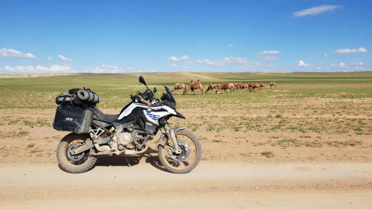  /></p><p>Mi-a plăcut mereu să trăiesc statistica, oricât de puțin sens ar avea acest început de text. Adică să văd eu, cu ochii mei, cât de înalt e muntele ăla faimos din Caucaz, ce înseamnă jungla columbiană sau cât de vastă e taigaua siberiană. Sau, căci tot ne-am adunat aici, cât de pustie e Mongolia. Pentru că datele oficiale ne spun că este. Într-un document publicat în 2021 de United Nations, Mongolia figurează „în acte” cu o suprafață de circa 1,5 milioane de kilometri pătrați și cu o densitate a populației de 2,1 locuitori pe fiecare kilometru pătrat. Drept comparație, România ar avea 83,1 locuitori pe kilometru pătrat, potrivit aceleiași surse. Bine, bine. Dar ce înseamnă, pe de-adevăratelea, asta? Că nu ne pierdem timpul citind aici ceea ce ne poate zice orice ciot de articol de pe Wikipedia. Știm și noi, o să spuneți, că Mongolia e „ditamai” țara și are puțin peste 3 milioane de locuitori. Cum se traduce asta în termeni interesanți pentru omul normal, om curios de planeta pe care trăiește până perfectează Elon Musk racheta cu care vom coloniza alte sfere îndepărtate?</p><p>O să încep așa: ați mers vreodată cu mașina sau motocicleta timp de o zi întreagă și să nu vedeți niciun semn al civilizației în care bucuroși și nerecunoscători ne bălăcim? Am mers eu, într-o vară din 2018, pe o motocicletă BMW F 850 GS, prin Mongolia. Am intrat în țară prin nord, din Rusia, absolut fără niciun plan. Google Maps nu există în Mongolia și pentru simplul motiv că, la vremea cu pricina, toată țara aia avea trei șosele. Una care o străbătea prin nord, una prin sud și una în construcție prin centru. De la vest la est sau invers, cum vreți. Altfel, legăturile între aceste șosele asfaltate se făceau pe… oriunde. Ăsta a fost primul șoc în Mongolia, momentul în care am înțeles că al nostru concept de proprietate privată nu există în afara orașelor și orășelelor. Practic, în traducere liberă, o iei pe unde îți vine, nene! Ca pe vremuri, pe modelul:</p><p>– Salut, Ioane!</p><p>– Salut, Gheorghe!</p><p>– Un’ te duci, Ioane?</p><p>– Uite să aduc iarbă la animale, Gheorghe!</p><p>– Păi de unde o iei? Încotro te îndrepți?</p><p>– Mă duc spre răsărit, încolo!</p><p>Cam așa e și cu Mongolia. Din Murun, din nord, astea sunt indicațiile pe care le primești de la localnici. „O iei încolo” și un semn din mână către sud. Păi, stai. Încolo, încolo. Dar pe unde? Încolo, românule! Ce nu ți-e limpede? Spre sud. Bun, mergem spre sud. Pe unde vezi cu ochii, pe oriunde, românule. Asta îmi spuneam eu singur în cască, încercând să depășesc uriașul obstacol mental de a călca sub anvelopele de offroad un pământ complet nepregătit pentru a fi străbătut. Pentru că Mongolia era, și din ce înțeleg încă este, așa cum ne-au lăsat nouă dinozaurii planeta acum multe milioane de ani. Adică a tuturor.</p><p>Pornesc. Drumul spre sud este o combinație de pâmânt, drum bătătorit cu nisip, gropi mici și pietre dese și ascuțite. Și, pe măsură ce mă îndepărtez de Murun, nimic mai mult decât un sătuc din sudul unui colosal lac cu apă dulce care comunică cu Baikalul rusesc, dispare și orice urmă de civilizație. Efortul depus e uriaș, nu e o suprafață făcută pentru a fi parcursă de motociclete, ci de caii hoardei lui Ginghis Han. Pasuri montane separate de podișuri înalte, verzi și drepte, văi pietroase și urcări bolovănoase. Și nimeni în jur. Dar nu „nimeni” ca de 1 ianuarie la 8 dimineața în București când ies hipsterii să facă poze pe Calea Victoriei. Nu, tati! Nimeni as far as the DJI Spark can see. Mers în regim de chin timp de patru ore până la prima întâlnire cu un suflet. Un păstor, nomad, care își dirijează turma de oi în jurul unei iurte lângă care fierbe un cazan uriaș, de facere chinezească, cu organe de ovină. O liniște „naturală” surprinzător de apăsătoare în care trebuie să faci orice altceva în afară de a te gândi unde ești. Nu ai voie, pentru binele tău, să te gândești că ești la ore de zbor distanță de primul spital sau, poate la fel de rău, la ore de zbor distanță de primul loc din care îți poți cumpăra o bucată de pâine, un măr sau un pahar cu apă. Fără semnal la telefon, doar cu speranța că dispozitivul conectat la satelit funcționează așa cum spune producătorul și că, în caz de apăsare a butonului SOS, cineva va veni.</p><p><strong>În cât timp parcurgi 200 de kilometri? În 10 ore!</strong></p><p>O primă zi în care, după aproape zece ore de mers pe motocicletă, am parcurs în jur de 200 de kilometri. Micile bucurii ale vieții, ca-n pozele cu „citate motivaționale” de pe Instagram, capătă noi valori. Mica bucurie se cheamă Tosontsengel, un cătun care are și un soi de hostel în care mă trântesc de îndată ce opresc motorul. Pentru echivalentul a 9 euro primesc o cameră simplă, cu pat și… fereastră. Și o baie pe hol, la comun. „Ațipesc un pic, apoi cobor să caut ceva de mâncare”, zic.</p><p>Zece ore a durat ațipitul. A doua zi de pustiu a început tot fără o țintă. Spre vest, teoretic. Practic, pe unde e drumul mai puțin distrus. Poteca, cărarea. Satelitul îmi arată că trebuie să fac dreapta, doar că dreapta arată înfiorător. Se vede la orizont un drum plin de gropi, de bălți, de noroaie. În față, deși cu semn de interzis, asfalt! Proaspăt, curat, încă nedat în folosință. Hai pe asfalt! Și îi dau! Pilot automat la 110 km/h și pace! Șoseaua asta nouă face un pic stânga, iar stânga înseamnă sudul Mongoliei. Cât de rău poate să fie? Habar nu am unde e sudul ăsta, nu trebuie să ajung acolo, dar nu mă dau jos de pe asfalt. Continuă plăcerea preț de vreo 80 de kilometri, după care jihad. Groapă lângă groapă! Nu pricep cum un drum de pământ poate avea atâtea gropi. Efortul depus e colosal, e dincolo de ceea ce credeam eu că poate duce corpul meu. Despre motocicletă, despre „fier”, nu mai vorbesc. Aș telefona la BMW, la Berlin, să le spun că n-au cum să fi testat modelul ăsta în condiții mai dure decât am făcut-o eu în Mongolia.</p><p>Rețeta peisajului e aceeași, nimic în jur, natură așa cum e de când hău’, cum spunea bunica. Și două întâlniri. Un cuplu de motocicliști cu care mă salut din mers și un alt băiat, singur, cu care mă salut de pe loc. Îl cheamă Max, e francez, și face drumul în sens invers față de mine. E desfigurat de la efort, are echipamentul julit și peticit, motocicleta la fel. A căzut de câteva ori. Rău. Pe dreapta are cutia distrusă complet, e prinsă cu fel de fel de improvizații. Și-a rașchetat carena, s-au smuls chestii de pe acolo.</p><p><strong>Atunci când banul e chiar ultima grijă din lume</strong></p><p>Cade toată lumea pe aici, cine sunt eu să nu fac la fel? Vreun Cyril Despres, vreun Mani Gyenes? Nu. Cad și eu. Linie dreaptă, teoretic. Practic, linie dreapta formată din S-uri șerpuite pe câmpie. Dâmb măricel în față, dar din cauza nisipului îl văd prea târziu. Motocicleta se ridică un pic de la sol, dar e sub control. Înălțimea e mică, am să aterizez fără probleme, mi s-a mai întâmplat. Doar că după dâmb e ditamai balta cu noroi. Mare, imposibil de evitat. Într-o fracțiune de secundă trag din corp roata față spre stânga și evit balta. Dar nu și cu spatele. Roata spate întră în noroi, alunecă, iar motorul care pe stânga. De la viteză mică, dar cade. Mă ridic rapid, opresc motorul și ridic motocicleta de 250 de kile cu tot cu bagaje dintr-o singură mișcare. Adrenalină! Am pus-o! Dacă s-a stricat ceva pe aici, am pus-o rău. Mă uit la far, e în regulă. Proiectoarele la fel, maneta de ambreiaj la fel, protecția la fel. E bine. Trecem la motor, e ok. Nu e ok pedala schimbătorului, e îndoită tare. Încerc să bag în viteză, merge! E bun. În rest, nimic!Sunt atât de departe de orice încât și adrenalina se simte diferit. Dacă la o căzătură în Apuseni mă gândesc că am julit o carnă și am rupt un schimbător de 300 de euro, aici banul nu are nicio importanță. Aici mă gândesc doar la supraviețuire și la faptul că dacă motocicleta nu mai merge, tragedia e la ea acasă. Ce fac? Cum dau de oameni? O iau pe jos? Cât? 100 de kilometri? 200? În ce direcție? Ce mănânc, ce beau? Cât ține corpul în condițiile astea? Dar am noroc, motocicleta merge. 14 ore de la momentul în care am mișcat roata pentru prima dată pe ziua cu pricina apare și primul oraș la orizont. Deschid telefonul și văd că sunt în Altai. Adică în sudul Mongoliei, la drumul asfaltat făcut de chinezi care duce spre vest, spre granița cu Rusia. 14 ore în care mi-au apărut în fața ochilor o mână de oameni, cu tot cu motocicliștii menționați anterior.</p><p>Două zile, pe calendar. 24 de ore de mers cu motocicleta. Puțin peste 500 de kilometri parcurși traversând Mongolia de la nord la sud, fără să-mi fi propus asta neapărat. Și, cu certitudine, cele mai grele condiții în care am mers vreodată pe două roți.</p><p><img data-lazyloaded=